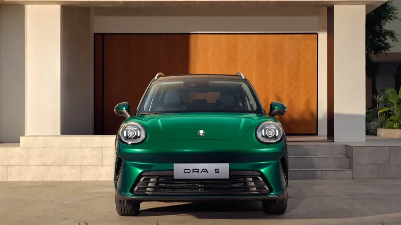 Elettronauti - GWM ORA 5 · Vista frontale di un’auto verde con fari circolari, parcheggiata davanti a un edificio moderno.